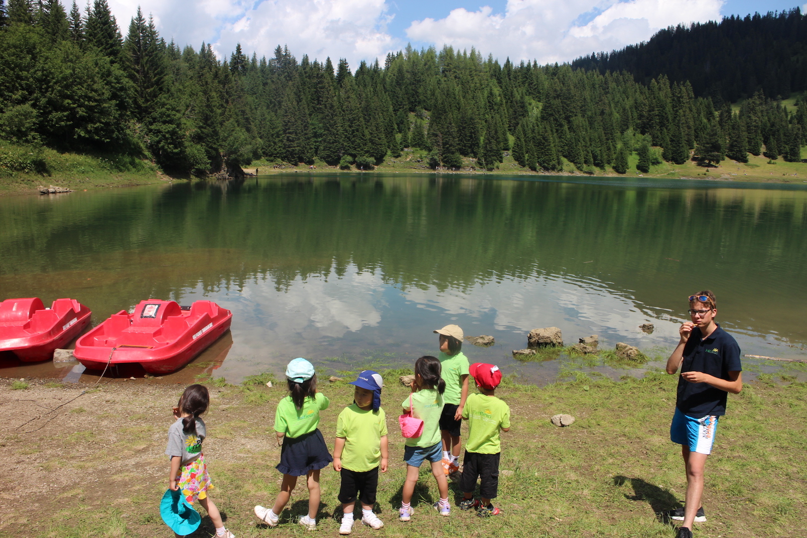 Small Alpine lake with pedal boats moored on the shore and a group arriving with a monitor