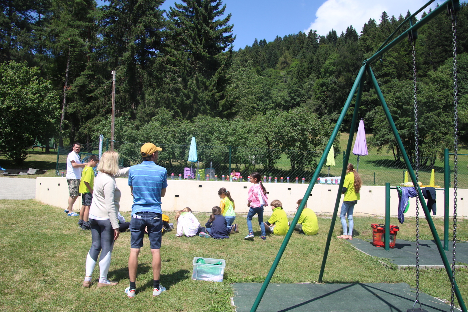 Outdoor play and swing area with staff and campers on the grass, forest and mountains behind